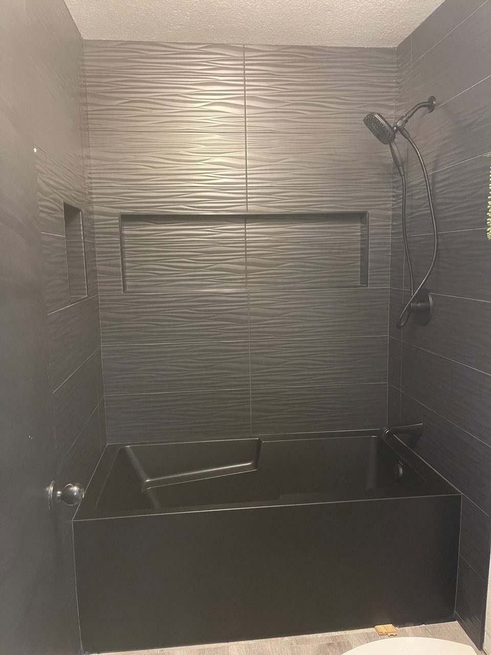 Finished tub and shower surround in grey textured wave tile with a black tub and handheld shower fixture