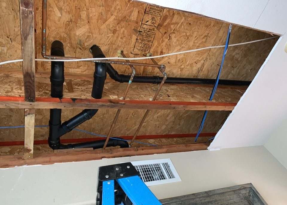 Black ABS drain lines and blue PEX water lines installed through open ceiling framing
