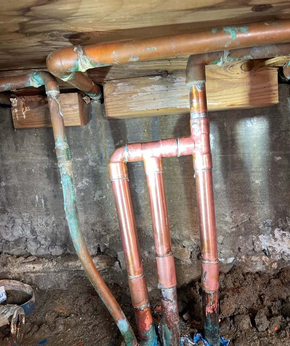 New copper supply manifold installed against a concrete foundation wall in a crawlspace