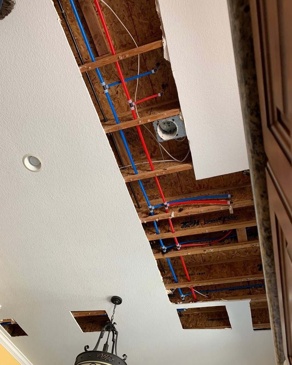 Red and blue PEX water lines running through open ceiling joists during a whole-house repipe