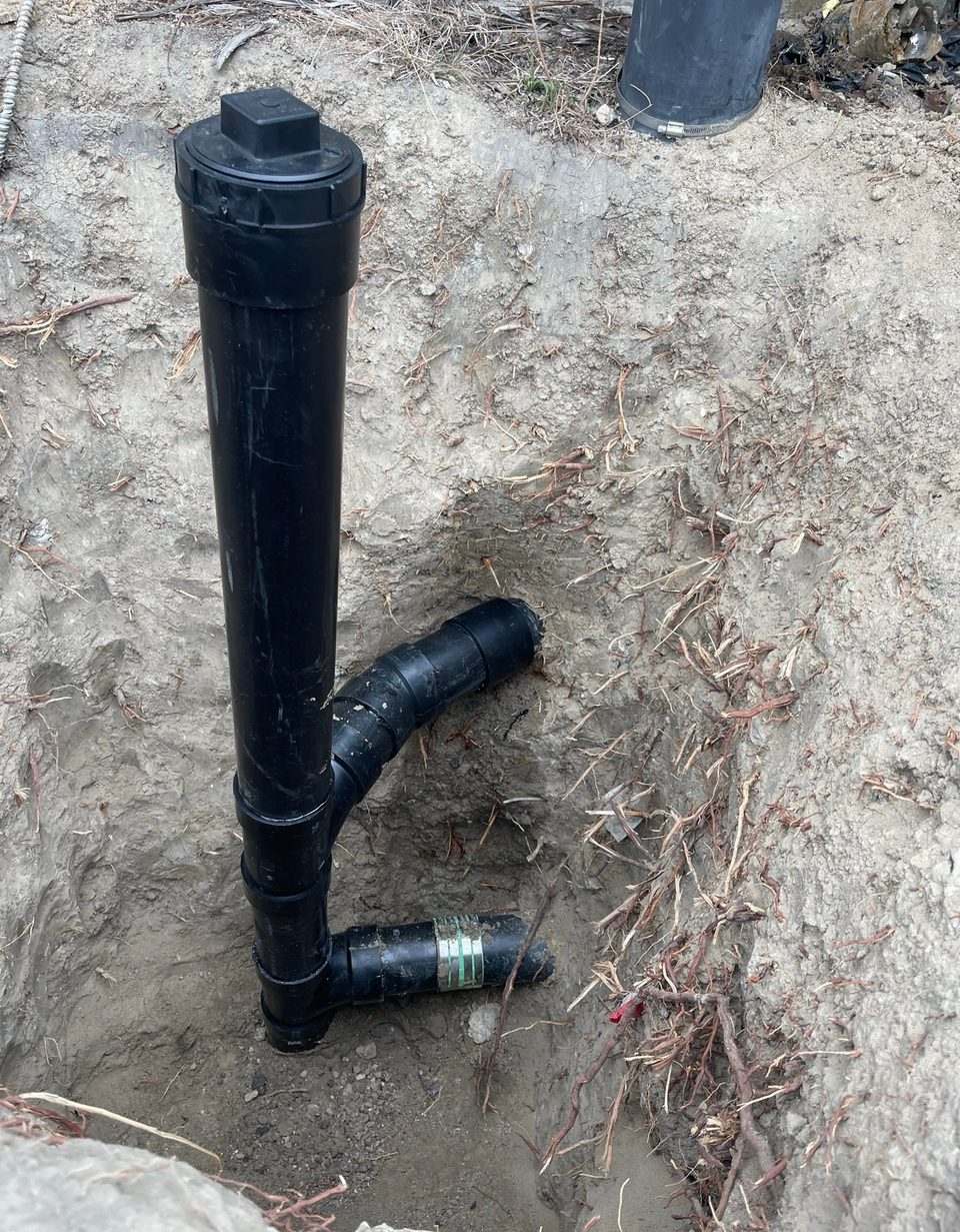Capped black ABS sewer cleanout riser installed on a new drain line in an excavated trench