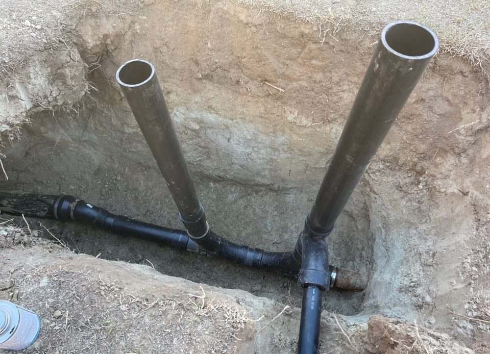 Pair of black ABS cleanout risers joined to a newly installed sewer line at the bottom of an open trench