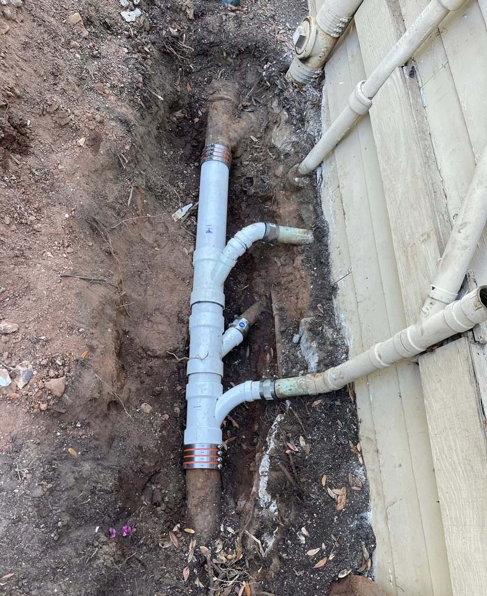Existing sewer line uncovered in a shallow trench alongside a building during a drain repair