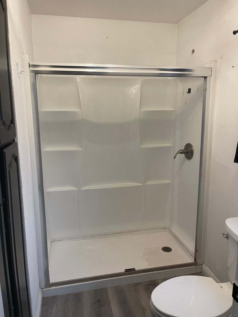 Newly installed white shower enclosure with sliding glass doors and a brushed nickel valve
