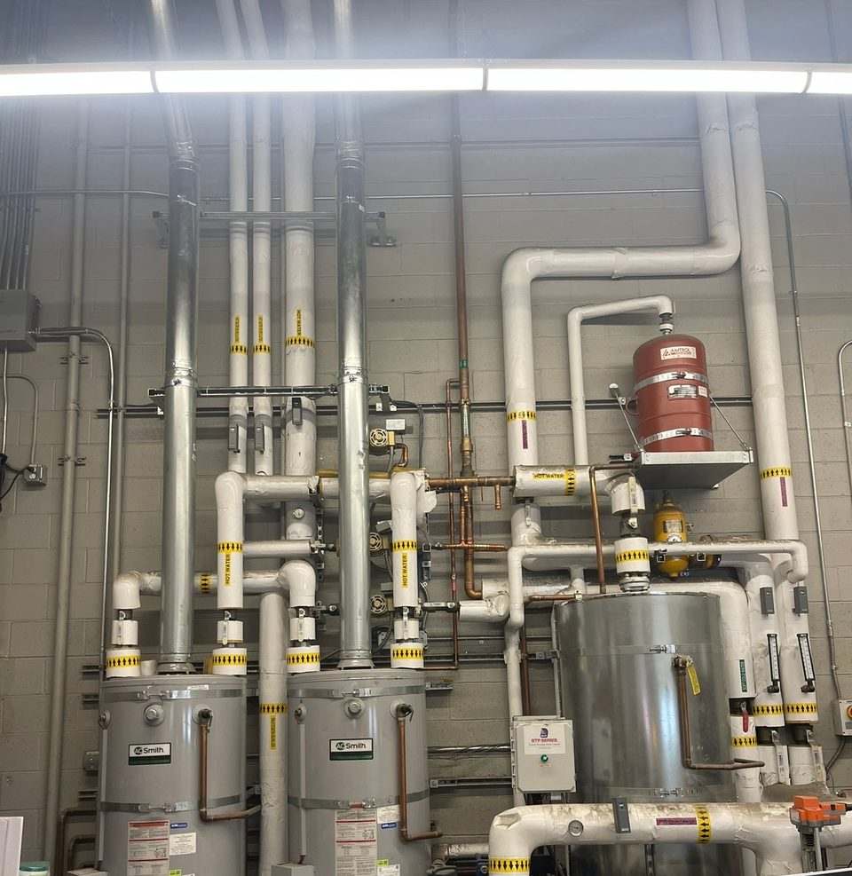 Bank of commercial water heaters with insulated supply piping, expansion tank and stainless storage tank in a mechanical room